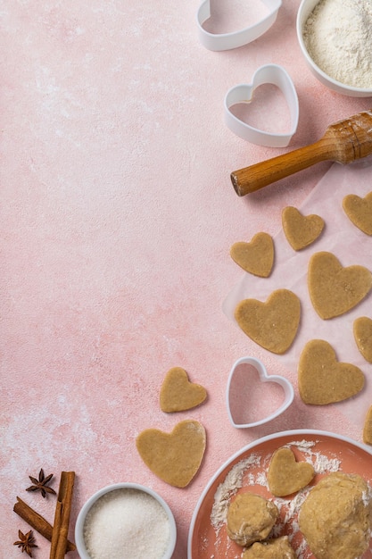 Cocinar galletas para el día de san valentín con ingredientes sobre un fondo rosa