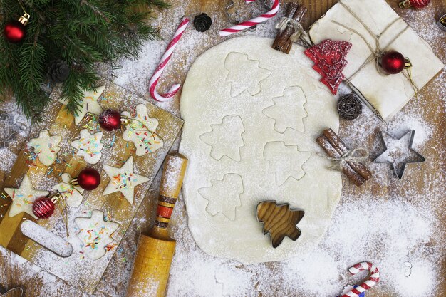 Cocinar galletas de mantequilla de diferentes formas en una mesa de madera con accesorios navideños