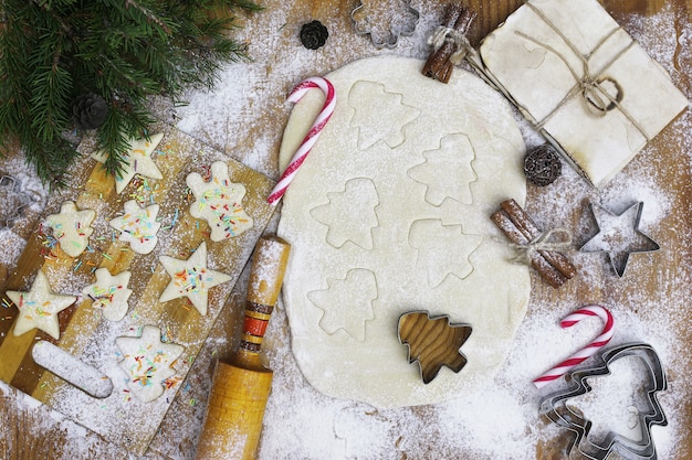 Cocinar galletas de mantequilla de diferentes formas en una mesa de madera con accesorios navideños