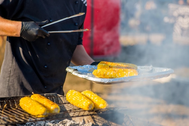 Cocinar con guantes freír maíz en una barbacoa abierta