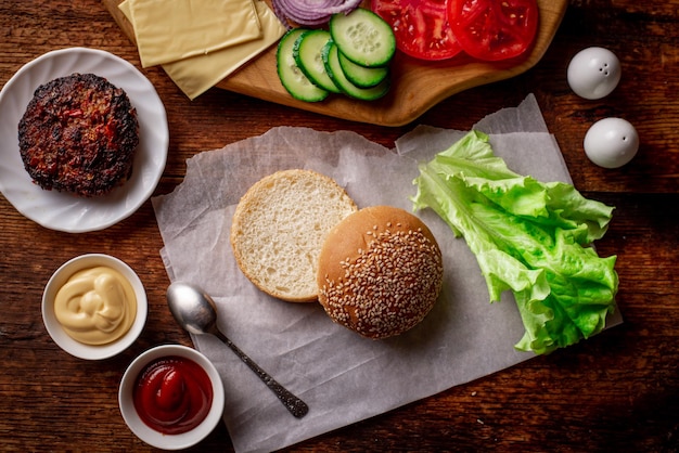 Cocinar hamburguesa o hamburguesa con queso Diferentes ingredientes para una hamburguesa clásica Carne a la parrilla verduras salsas verdes cerca de un bollo de sésamo Fondo de madera