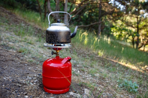 Cocinar hervidor de camping en una botella de gas rojo.