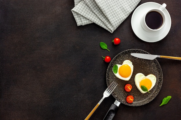 Cocinar huevos fritos en forma de corazón en una sartén con tomates y verduras