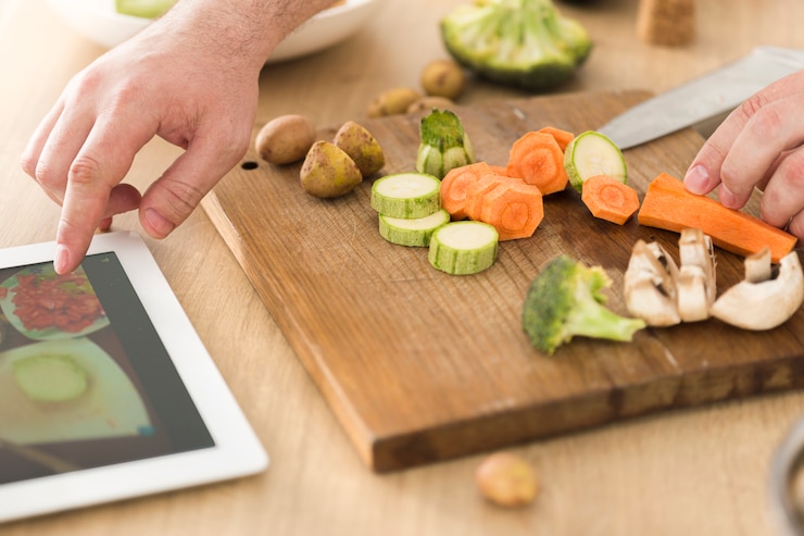Foto cocinar en línea o aprender el concepto de cocina. hombre preparando un plato vegano mientras mira la receta en internet usando una tableta