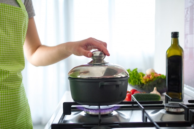 Cocinar a mujer en delantal de pie cerca de la estufa y cocinar sopa para la cena