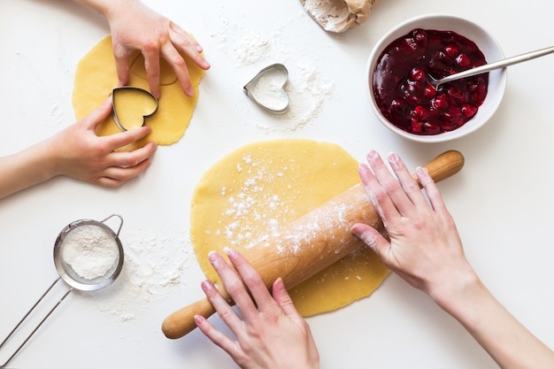 Foto cocinar con un niño. madre rueda la masa e hija hace galletas