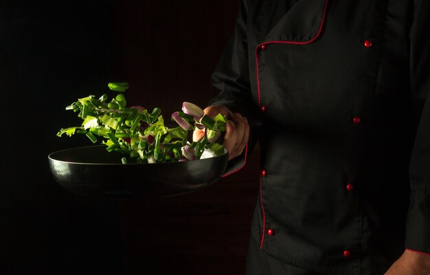 Cocinar o freír verduras frescas en una sartén sartén con verduras voladoras en la mano del chef concepto de dieta de verduras en fondo oscuro