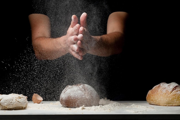 Cocinar pan. Manos con salpicaduras de harina y volando sobre mesa blanca cubierta con harina de sus manos. Chef aplaudir la mano del hombre de polvo de harina blanca sobre fondo negro. Espacio para texto. El concepto de nutrición