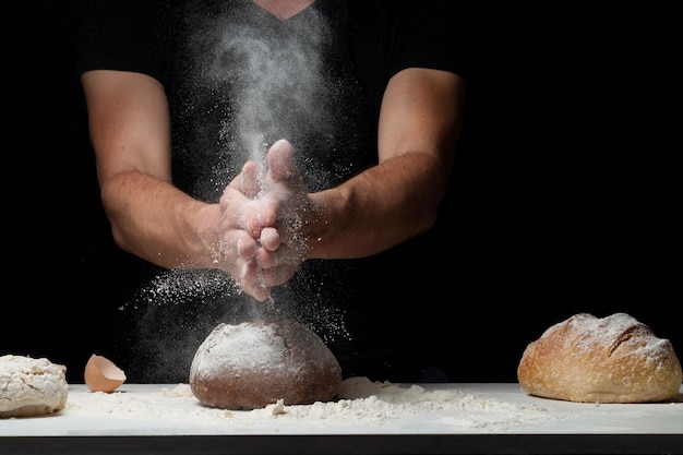 Cocinar pan. Manos con salpicaduras de harina y volando sobre mesa blanca cubierta con harina de sus manos. Chef aplaudir la mano del hombre de polvo de harina blanca sobre fondo negro. Espacio para texto. El concepto de nutrición