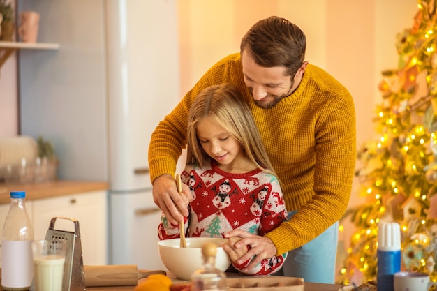 Cocinar con papá. Niña y su papá revolviendo algo en un bol