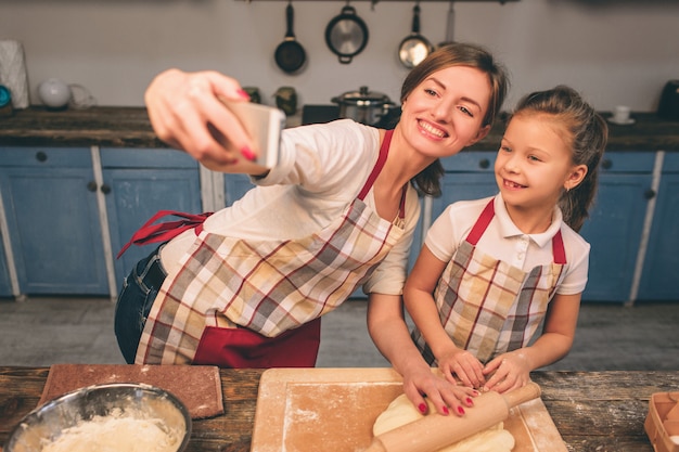 Cocinar pasteles caseros. Feliz familia amorosa están preparando panadería juntos. Madre e hija hija están cocinando galletas y divirtiéndose en la cocina. Envuelve la masa. Haciendo selfie