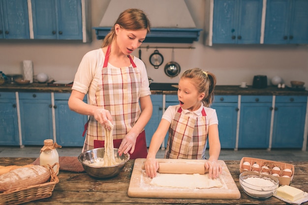 Cocinar pasteles caseros. Feliz familia amorosa están preparando panadería juntos. Madre e hija hija están cocinando galletas y divirtiéndose en la cocina. Envuelve la masa.