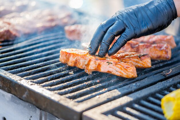 Cocinar pescado a la barbacoa Las manos enguantadas dan vuelta a los trozos de pescado a la parrilla