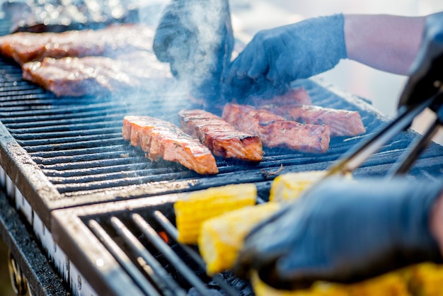 Cocinar pescado a la barbacoa Las manos enguantadas dan vuelta a los trozos de pescado a la parrilla