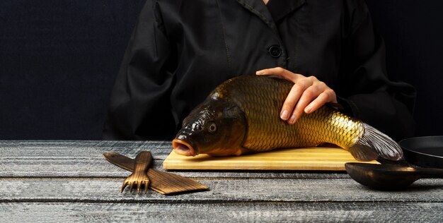 Cocinar pescado fresco de carpa dorada sobre una tabla de cortar sobre una mesa de madera negra con espacio de copia