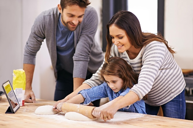 Foto cocinar pizza y familia en la cocina con tableta para la guía de recetas y mamá y papá aprendiendo con el niño enseñar a hornear y la niña ayudando a los padres con el rodillo en casa y juntos para la cena