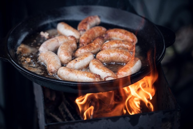 Cocinar salchichas al fuego en una sartén grande al aire libre