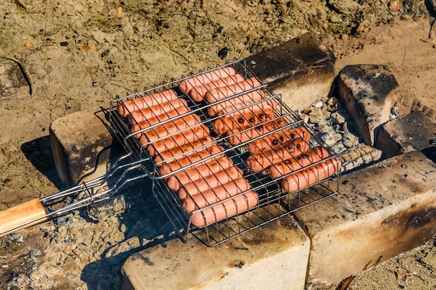 Cocinar salchichas en una parrilla en fogata