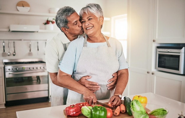 Cocinar verduras abrazar y pareja de ancianos con ingredientes de cocina preparar comida o sonreír en una cita romántica en casa Amor matrimonial nutricionista y hombre hambriento mujer o personas unidas por una comida saludable