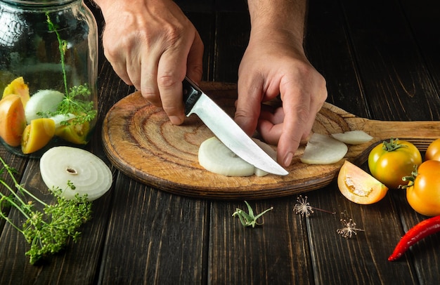 Cocinar verduras en escabeche en un frasco cocinero corta la cebolla con un cuchillo en la tabla de cortar de la cocina