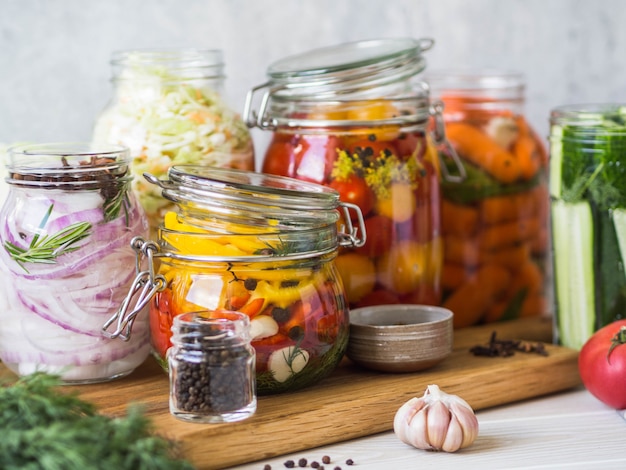 Cocinar verduras en escabeche. Salazón de varios vegetales en frascos de vidrio para almacenamiento a largo plazo. Conserva las verduras en frascos de vidrio. Variedad de vegetales verdes fermentados en tablero de madera