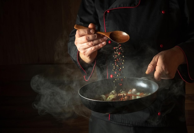 Cocinar verduras frescas El cocinero añade pimienta a una sartén humeante La idea de la cocina europea para un hotel con espacio publicitario