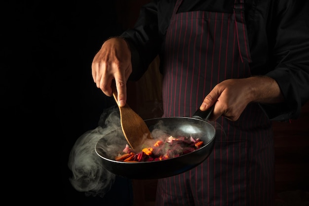 Cocinar verduras en una sartén caliente en manos de un chef Gastronomía o cocina molecular