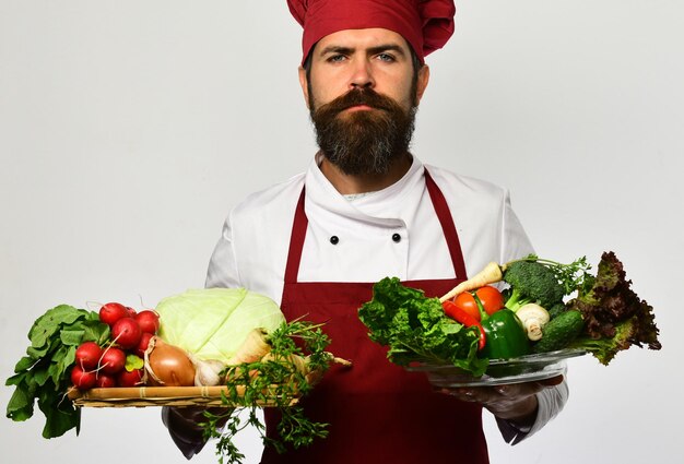 Cocine con cara seria en uniforme burdeos tiene ingredientes de ensalada