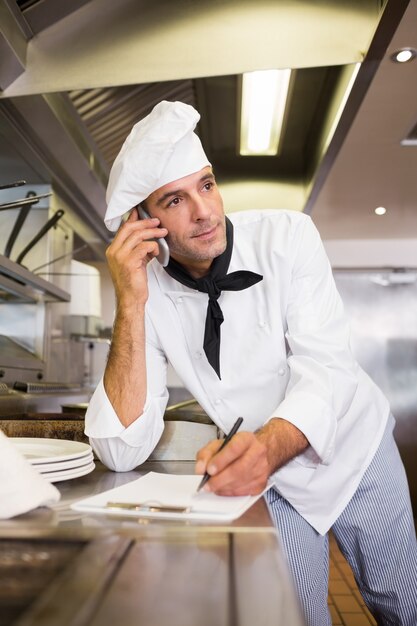 Cocine escribiendo en el portapapeles mientras usa el teléfono celular en la cocina