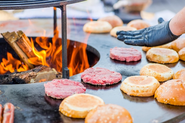 Cocine las manos en guantes a la parrilla empanadas de carne de hamburguesa en la parrilla Abra fuego en la barbacoa