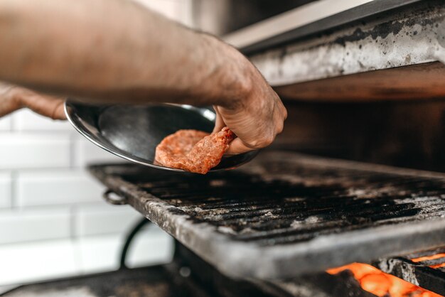 Cocine las manos pone la carne en el horno grill, cocina hamburguesa. Proceso de preparación de hamburguesas, comida rápida, barbacoa