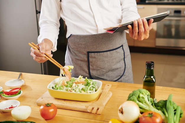 Cocine mezclando ensalada con palillos