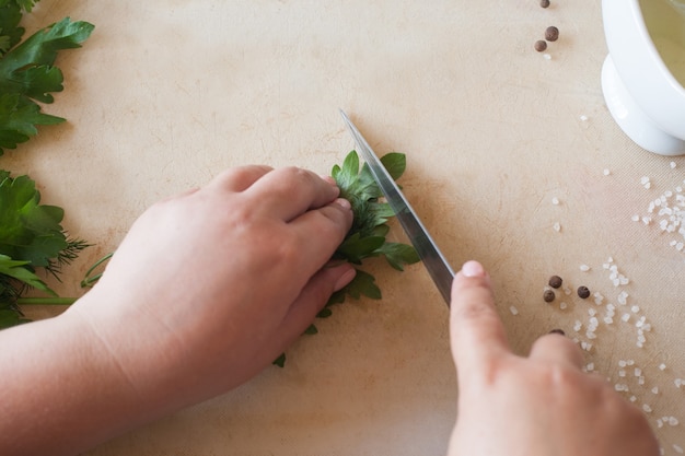 Cocine a la mujer cortando el perejil verde en el escritorio de madera.