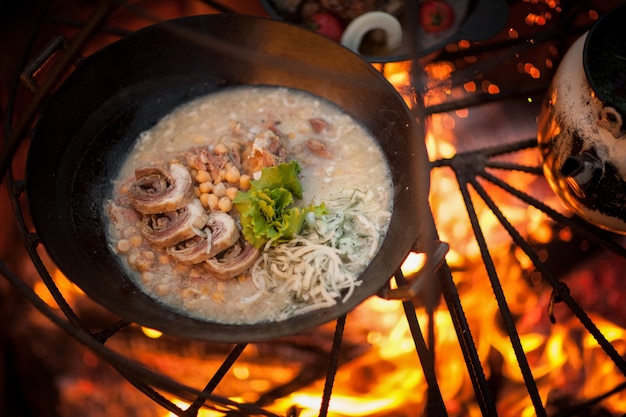 Cocine un plato de carne con guisantes en la hoguera con ramas de abeto.