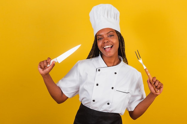 Cocinera afro brasileña joven sosteniendo cuchillo y tenedor para barbacoa preparándose para cocinar