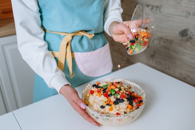 La cocinera agrega frutas confitadas a la masa. El proceso de mezclar ingredientes para pasteles en la cocina del hogar