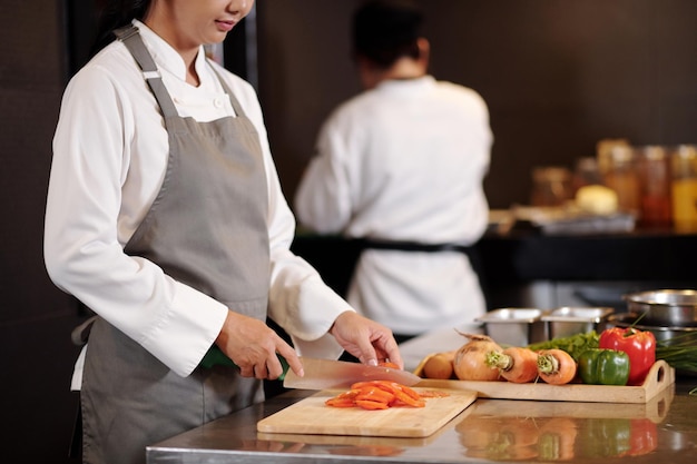 Cocinera cortando tomates mientras cocina ensalada en la cocina del hotel