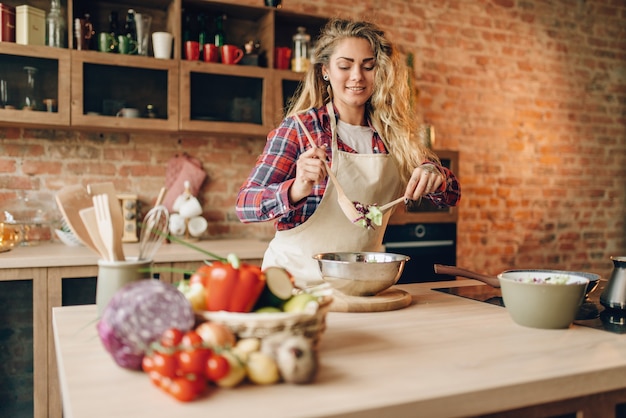 Cocinera en delantal prepara ensalada fresca