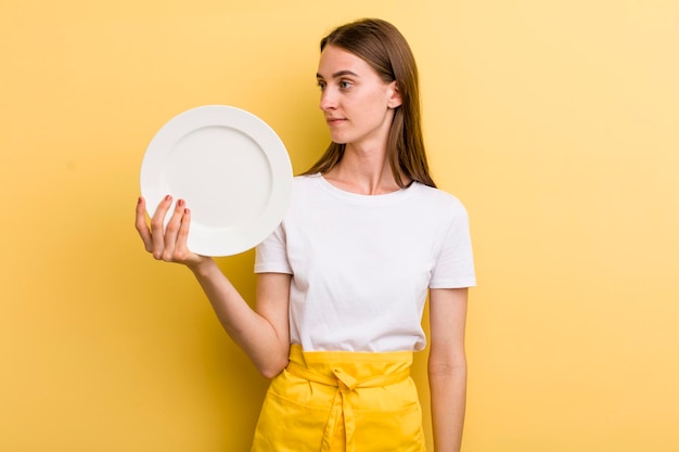 Cocinero adulto joven de la mujer bonita con un plato vacío