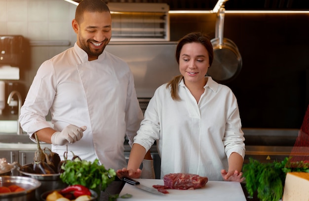 Cocinero africano joven hermoso está cocinando junto con la novia del Cáucaso en la cocina Un cocinero enseña a una niña a cocinar. Hombre y mujer cocinando en cocina profesional. relación interracial