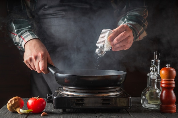 El cocinero agrega sal mientras cocina los alimentos en la sartén.