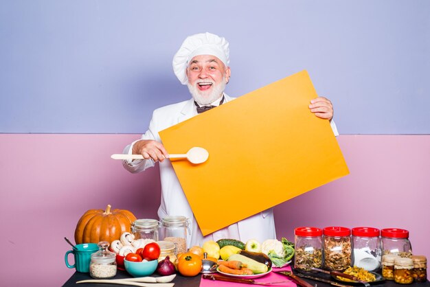 Cocinero asombrado que señala la cuchara en el menú del tablero en blanco profesión de cocina publicidad y concepto de personas m