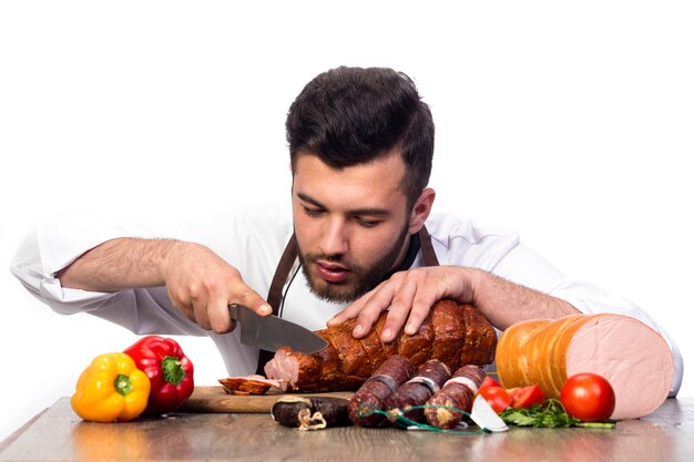 El cocinero corta la carne ahumada, también hay carne y pimienta en la mesa