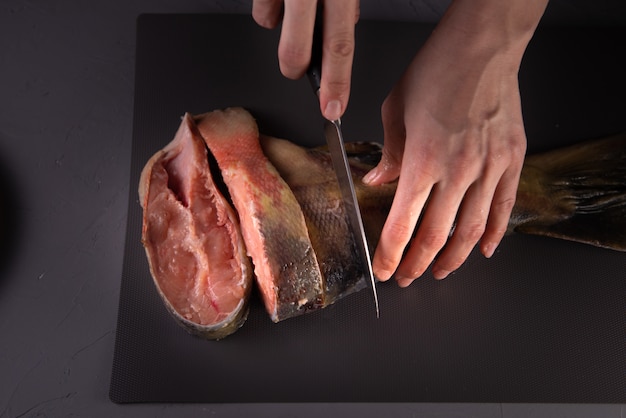 Foto el cocinero corta el pescado en trozos con un cuchillo sobre una tabla gris