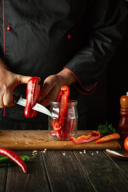 El cocinero corta pimientos para enlatar en un frasco Las manos de un cocinero con un cuchillo en la mesa de la cocina cortando capsicum Concepto de cocina de platos vegetarianos