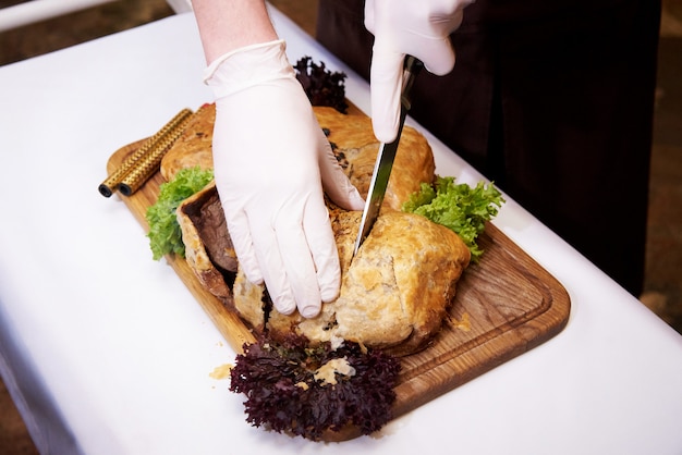 El cocinero corta el plato caliente cocinado en una bandeja en un restaurante.