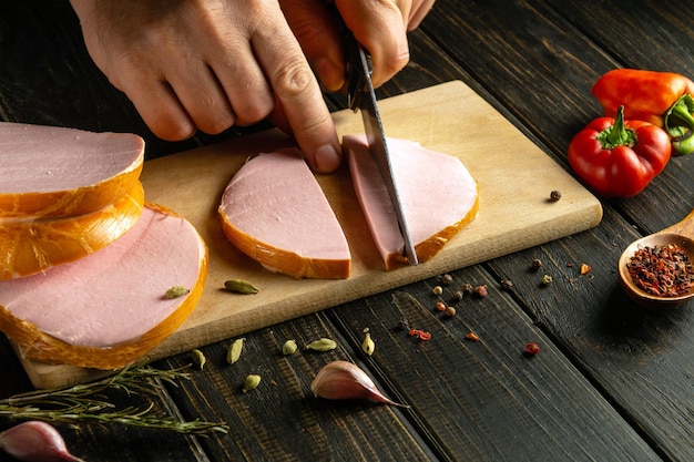 Foto el cocinero corta la salchicha escaldada en pedazos pequeños para hacer sándwiches.