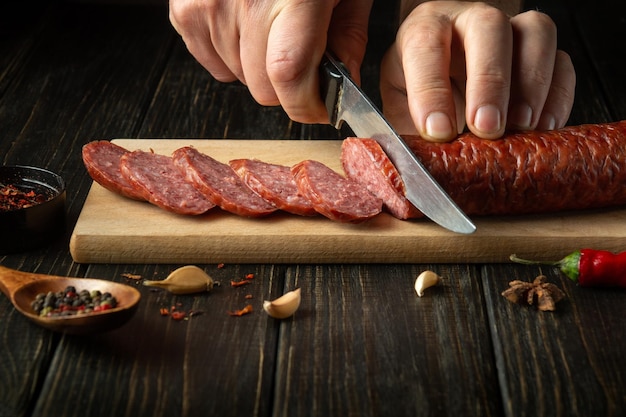 El cocinero corta salchichas caseras en una tabla de cortar de madera Cocina deliciosos sándwiches para un refrigerio en casa