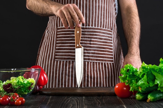 Cocinero. Cuchillo de chef profesional que incluye verduras frescas variadas sobre fondo negro