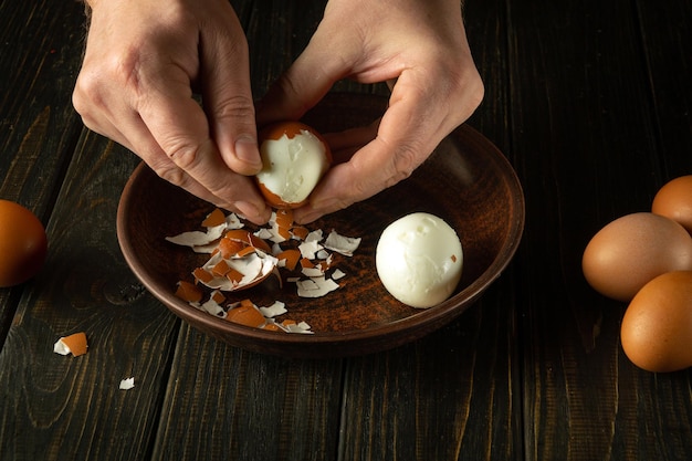 Un cocinero descasca un huevo cocido de su cáscara en la mesa de la cocina con sus manos conceptos de dieta de huevos blancos saludables espacio publicitario